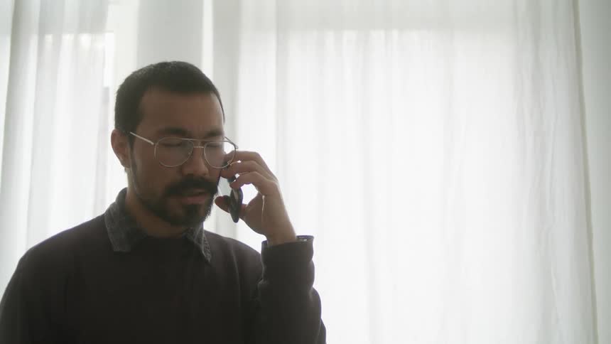 A man talks on his smartphone while standing in front of a large window