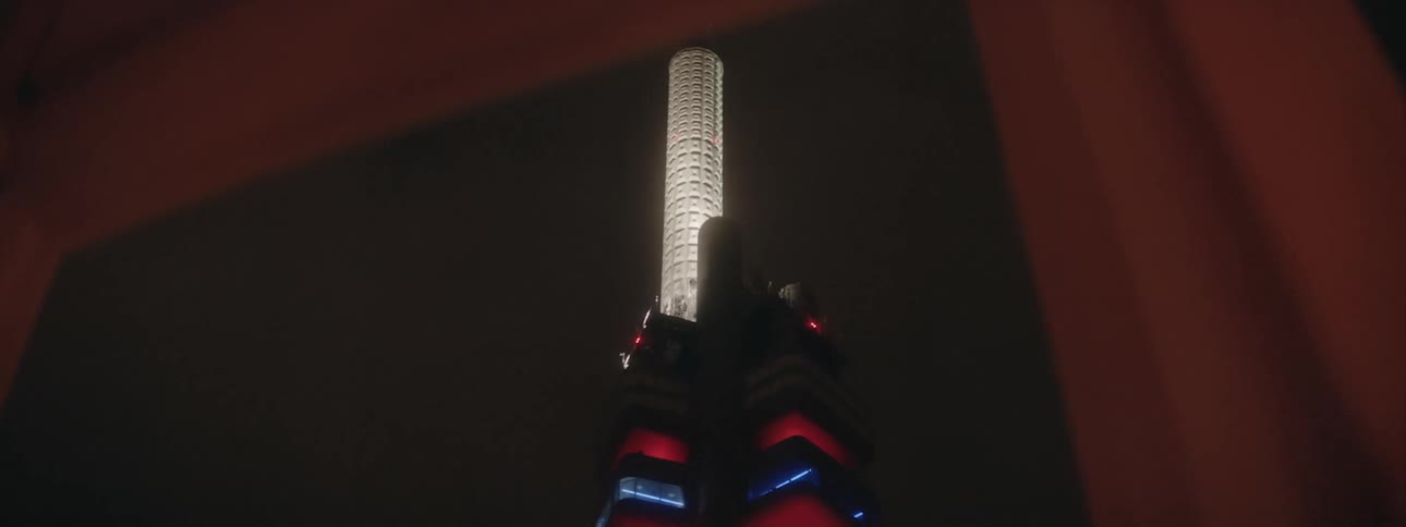 A tall illuminated skyscraper seen from a window at night