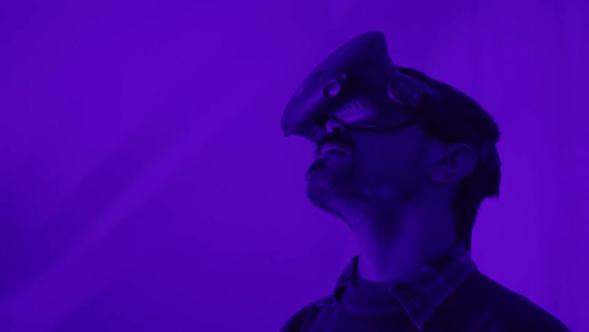 A man with a vr headset in a room with purple lights with a plant in the background