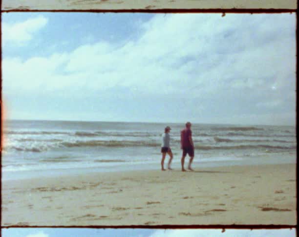 A man and a woman walking on a beach with the ocean sky and clouds in the background