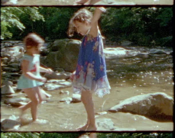 Two young sisters splashing and playing in a shallow river on a sunny summer day