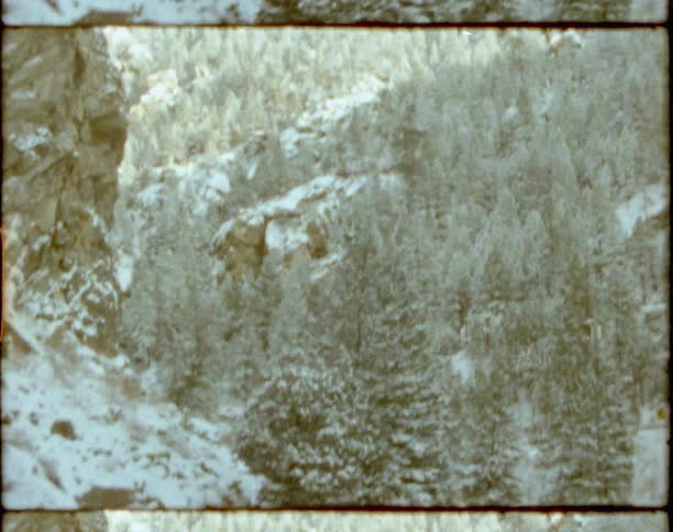 Vintage footage of a river flowing through snow at the base of a tree covered mountain