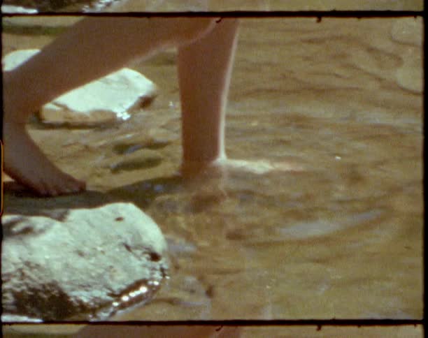 Vintage film of a person walking off of rocks in to a river