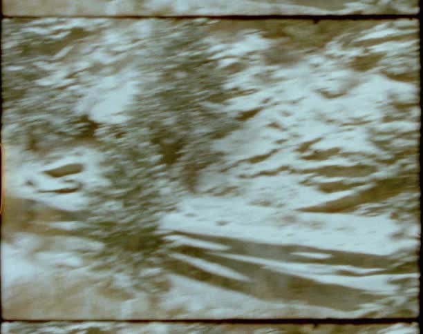 A father holds a babys hand while walking outdoors in nature in the snow next to mountains and a slope of trees