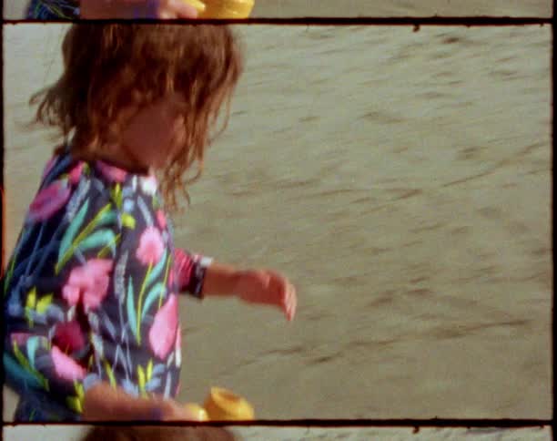 A child walks on the beach and pours water from a pale