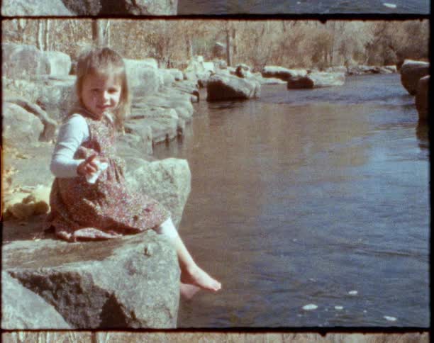 Young barefoot girl wearing a dress sitting over a rock near a river at daytime