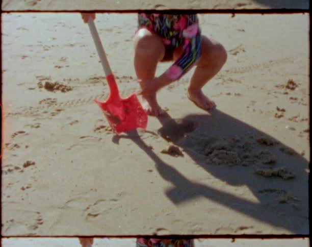 Little girl digging at the beach with a large plastic sand shovel