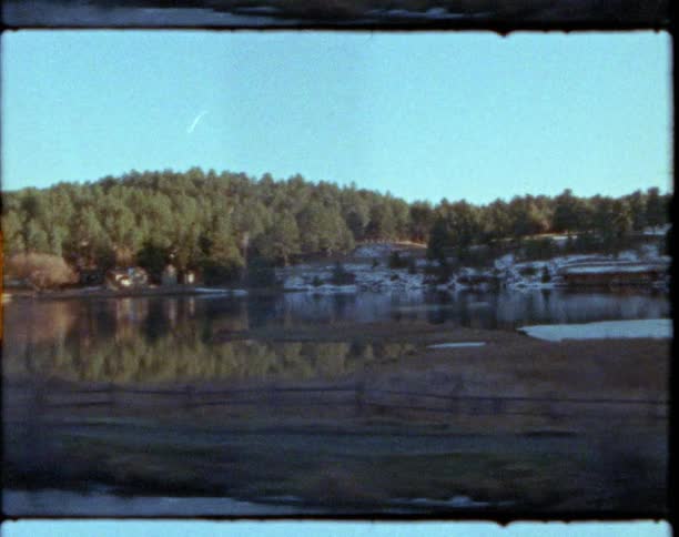 A lake surrounded by forest and hills under a clear daytime sky