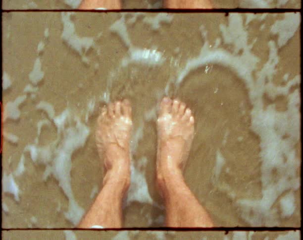 Man standing over the wet beach sand while waves wash over his bare feets