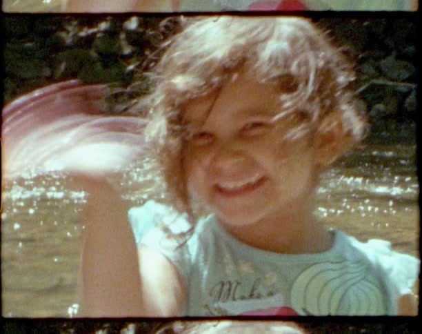A little girl waving with a river and plants in the background