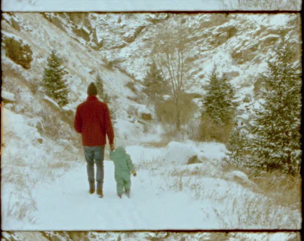 A man holding a childs hand and walking in the snow with trees in the background