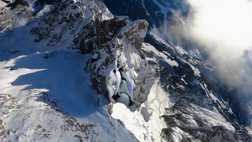 Person wearing suit glides over sharp sheer mountain ridge