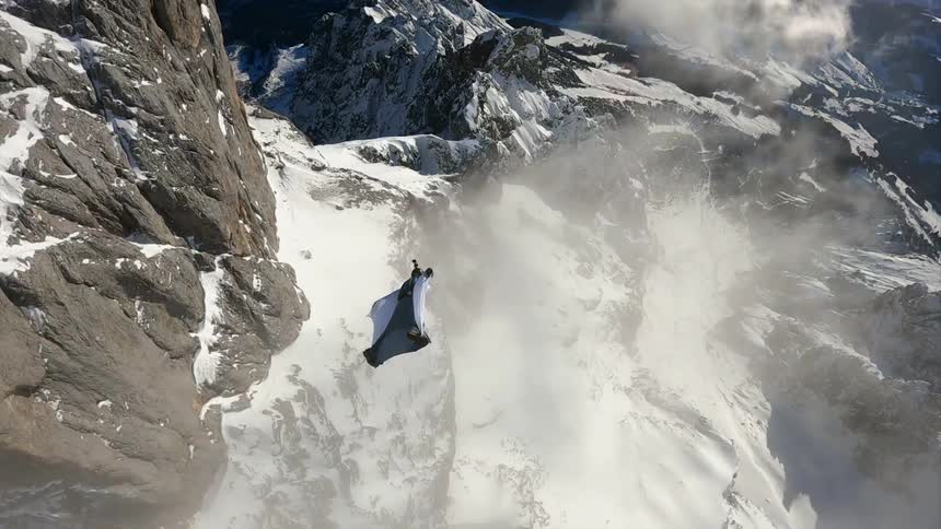 Person wearing a wing suit is gliding over a snow covered mountain canyon