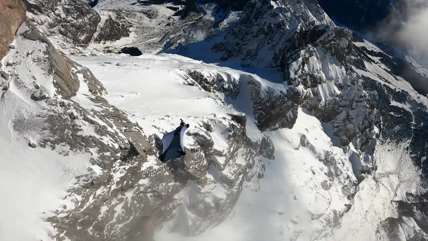 Person in wing suit flying around snowy mountain tops