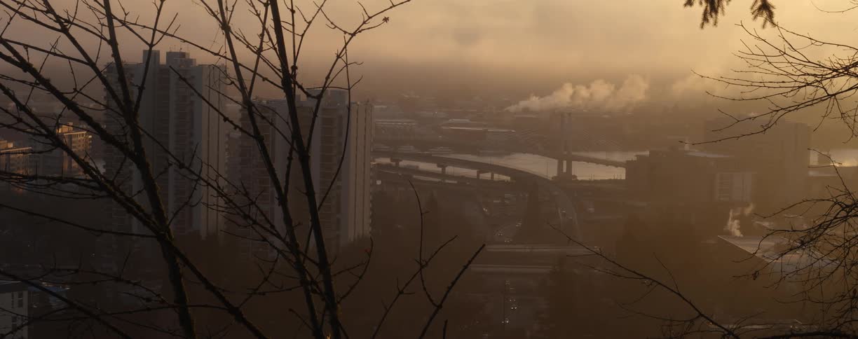 Cars travel on city highways and roads while smoke billows from factories