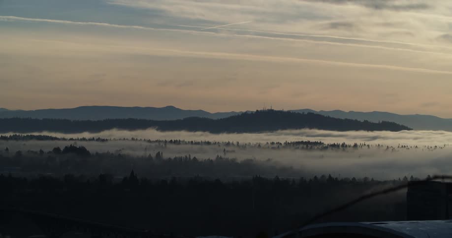 Fog flows over mountain and forest on other side of bridge