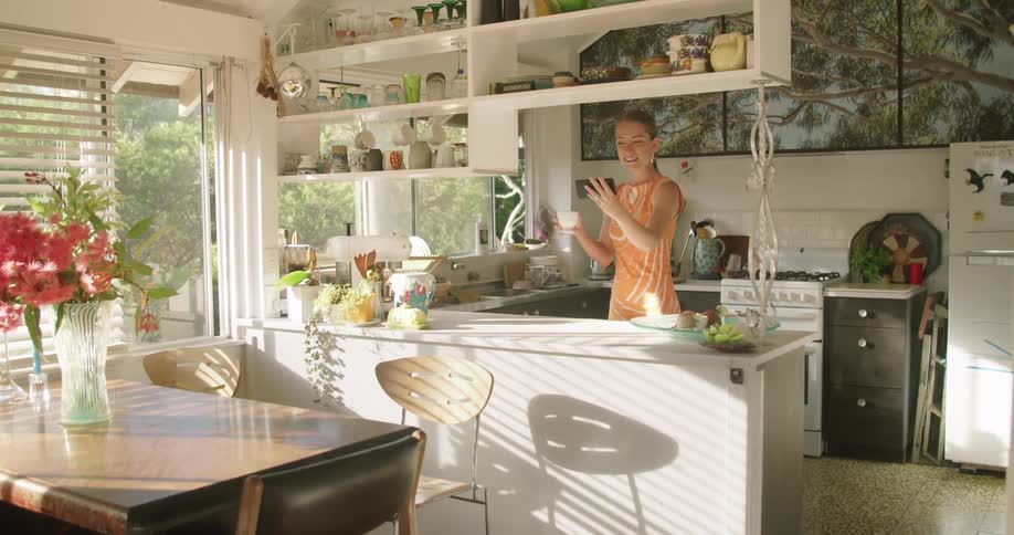 Woman standing in kitchen on mobile phone blows kiss at screen