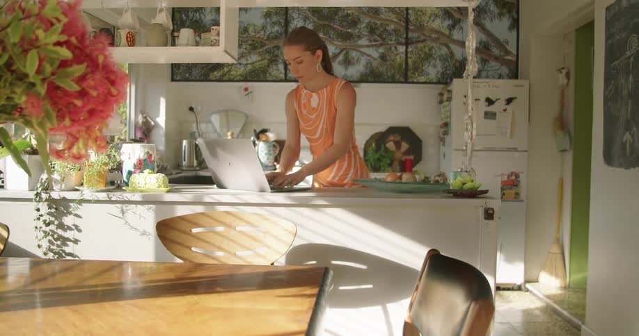 A woman typing on a laptop in a kitchen