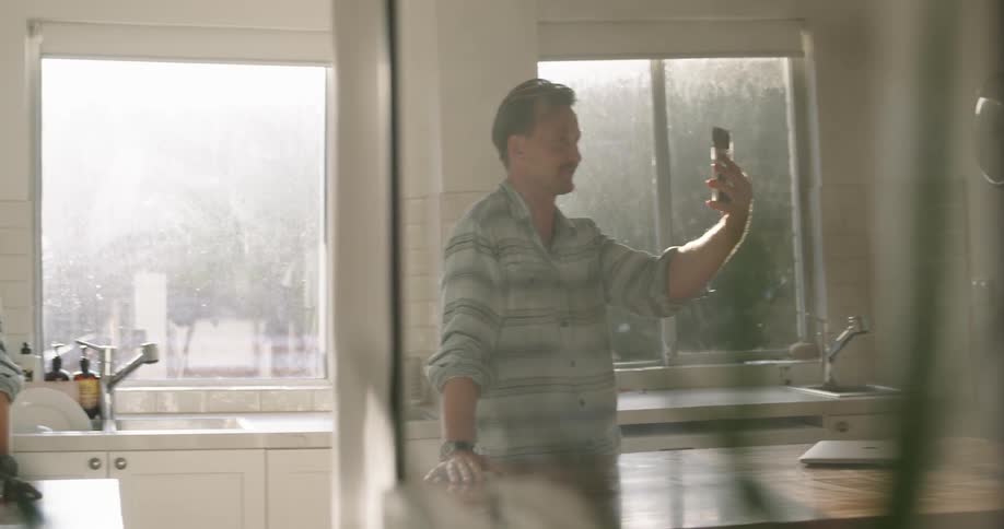 Man standing in kitchen video calling blows kiss at phone