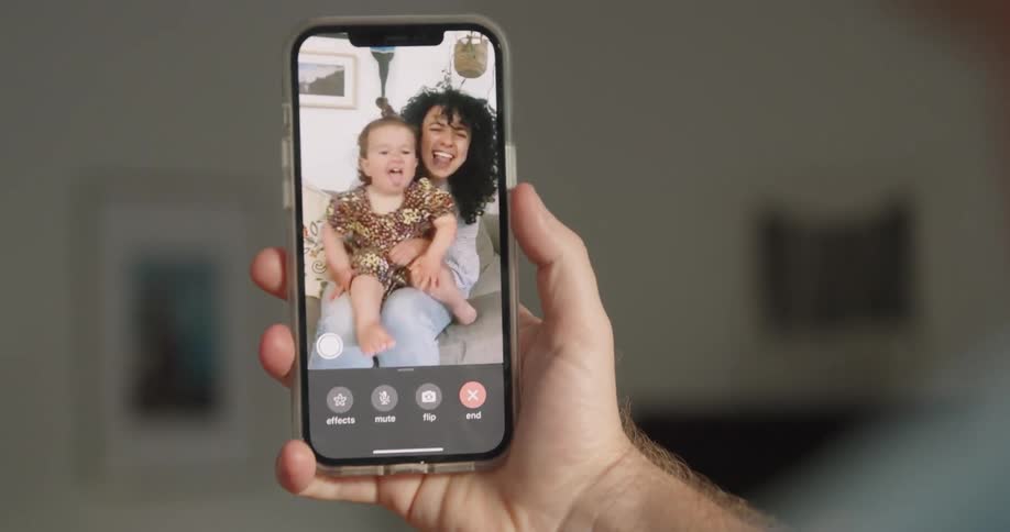 A man waves at his toddler daughter and wife during a video call on his smartphone