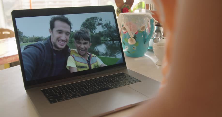 A father and son waving and smiling while boating on video chat