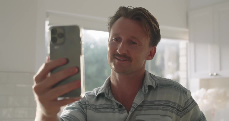 A man is standing in his kitchen with a cell phone