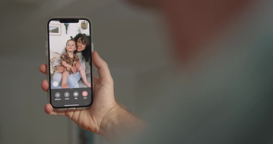 A man holds a cell phone as he video chats with his wife and daughter