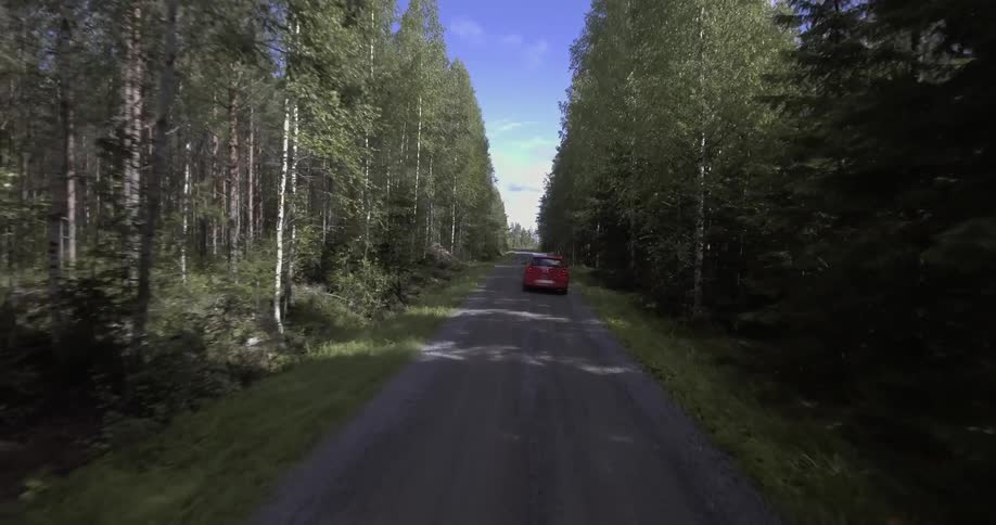 A red car drives down a small road