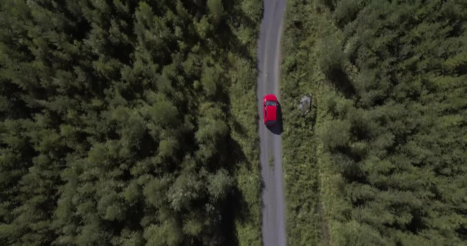 Aerial view of a red car driving down a small road
