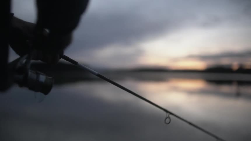 A person is wheeling in some line on a fishing pole at sunset