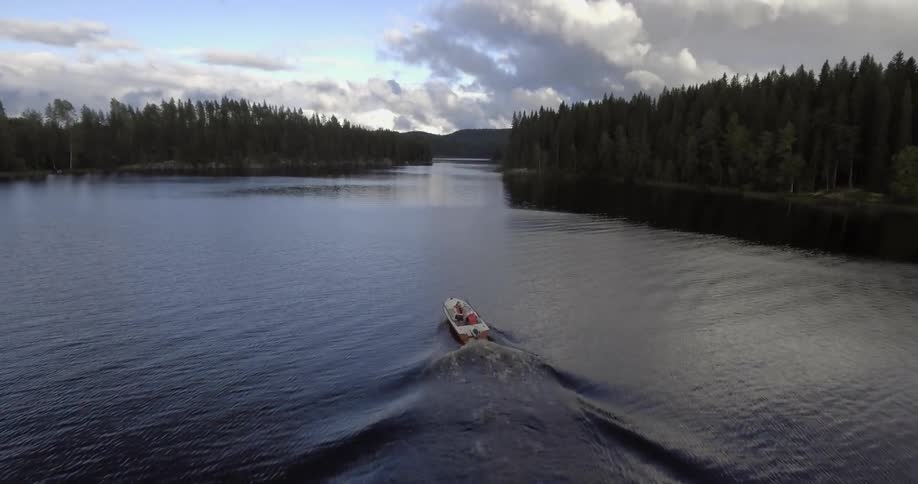 A boat travelling on a tree-lined, mountain lake