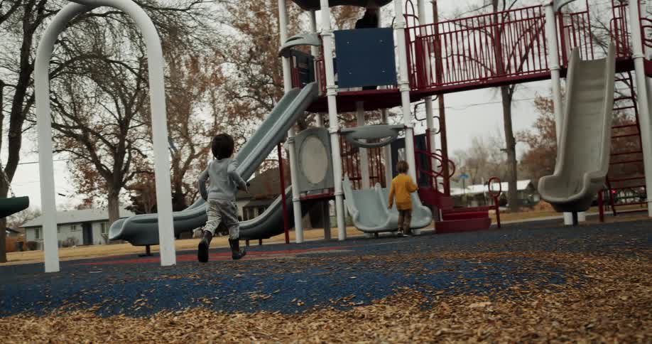 Two children running towards a playground with trees and houses the sky and clouds in the background