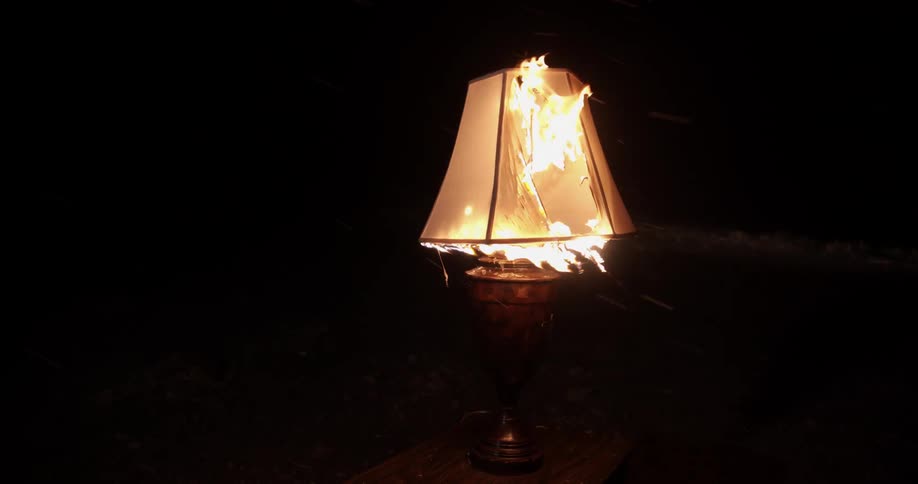 A lampshade on a ceramic base burns outside at night