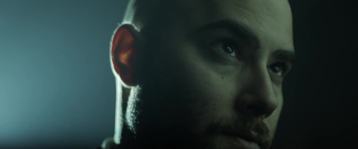 A man raises his eyebrow slightly as he stares with a soft light glowing behind him
