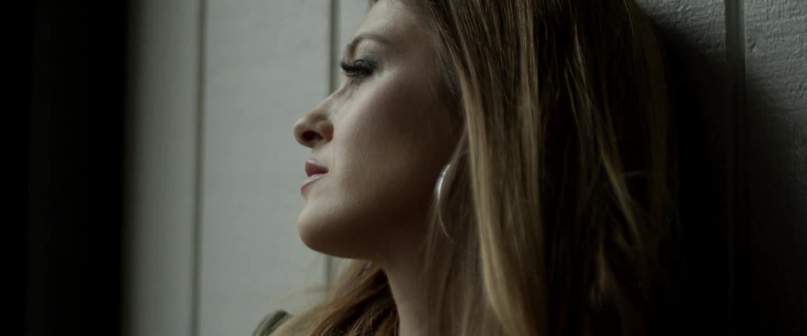 A woman sits against a wall outside as wind blows through her long hair