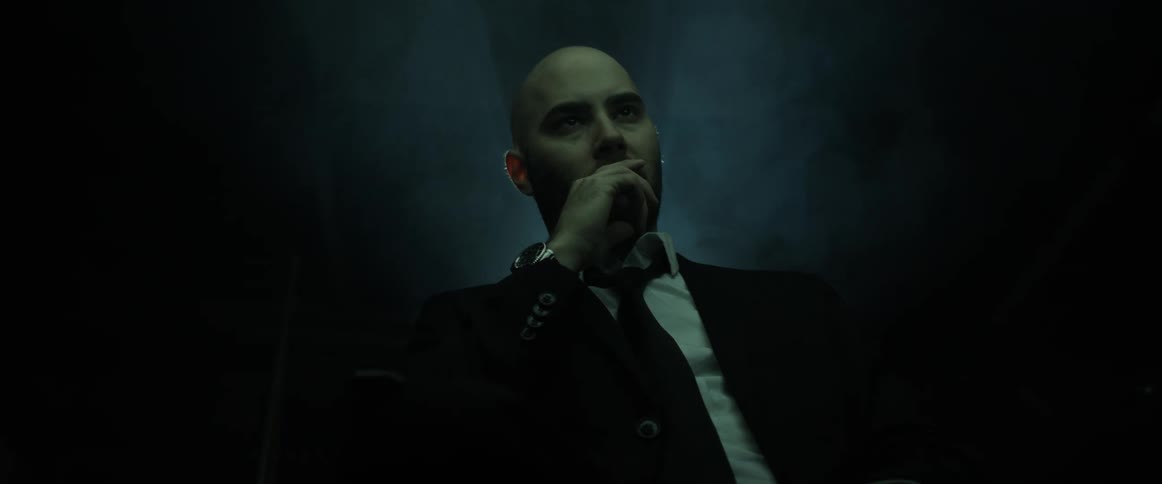 A man with a suit a tie and a wristwatch in a room with a projector in the background