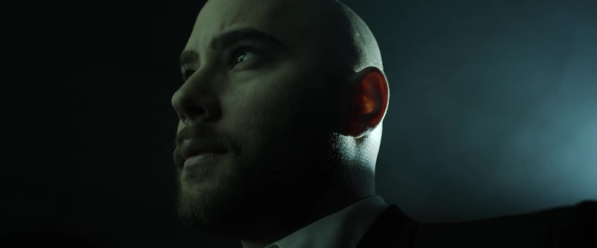 A man stares straight ahead as a projector flashes and changes color behind him