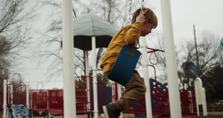 A boy swings on swing set in a playground on a cloudy day