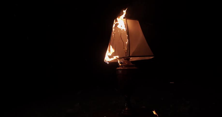 A shade atop a lamp burns in a dark room