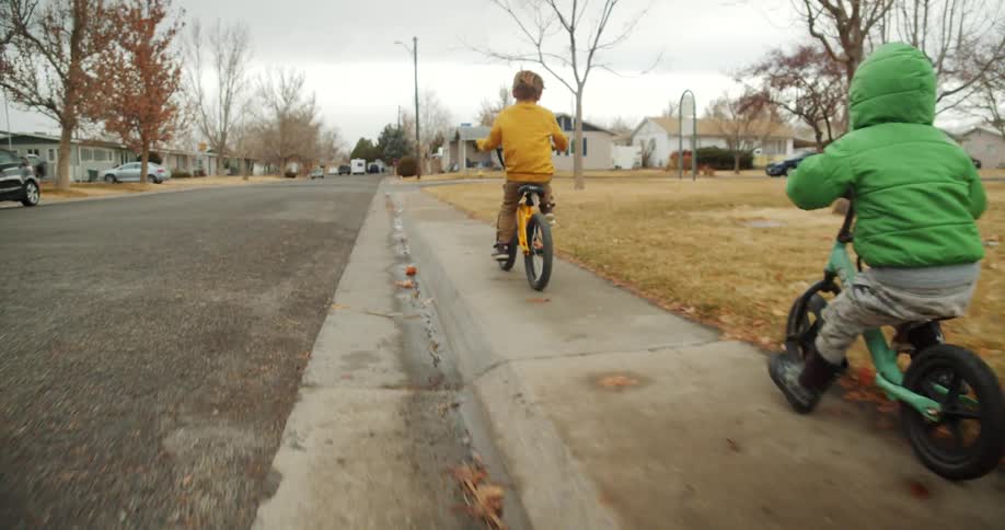 Two young boys riding bikes on a neighborhood sidewalk on a chilly day