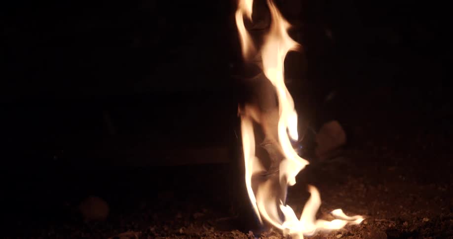 Fire and flames burning the leg of a table standing on a dirt yard at night