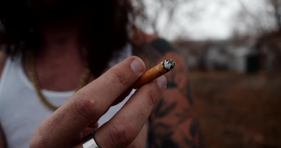 A man with a tattoo sleeve smokes a cigarette while standing outside his neighborhood