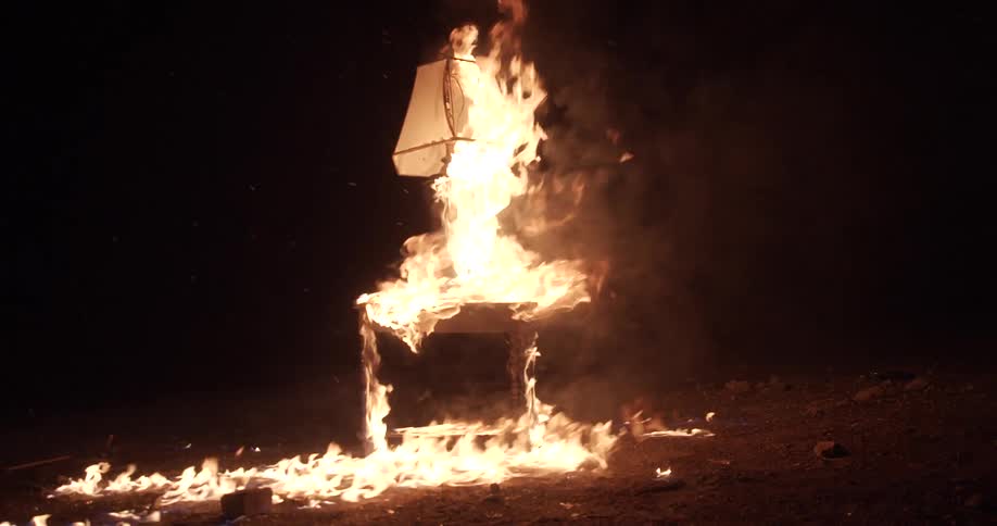 Fire and flames burning a desk and a lamp standing on a dirt yard at night