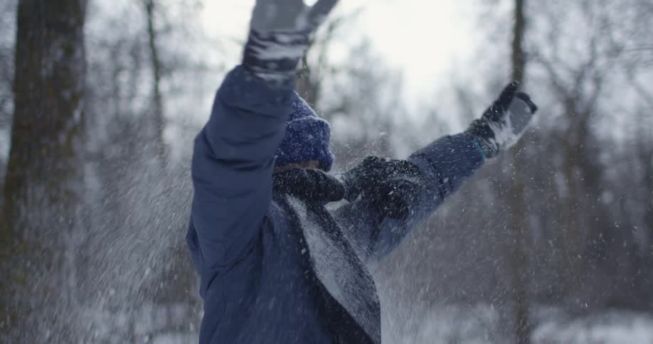 A young boy stands outside and throws some snow in the air