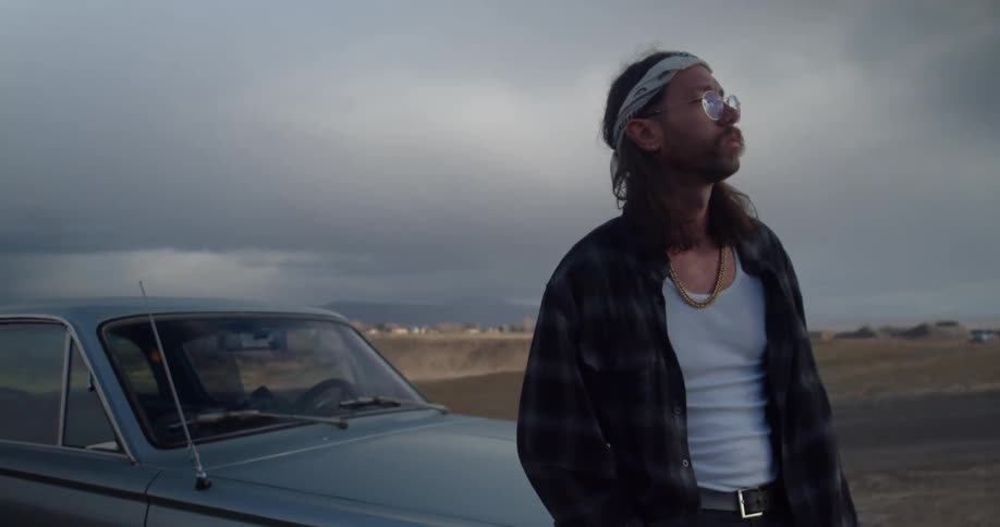A man stands against the hood of his car while parked on the side of the road