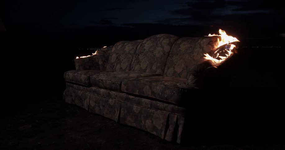 Sofa burns outdoors at night under cloudy sky