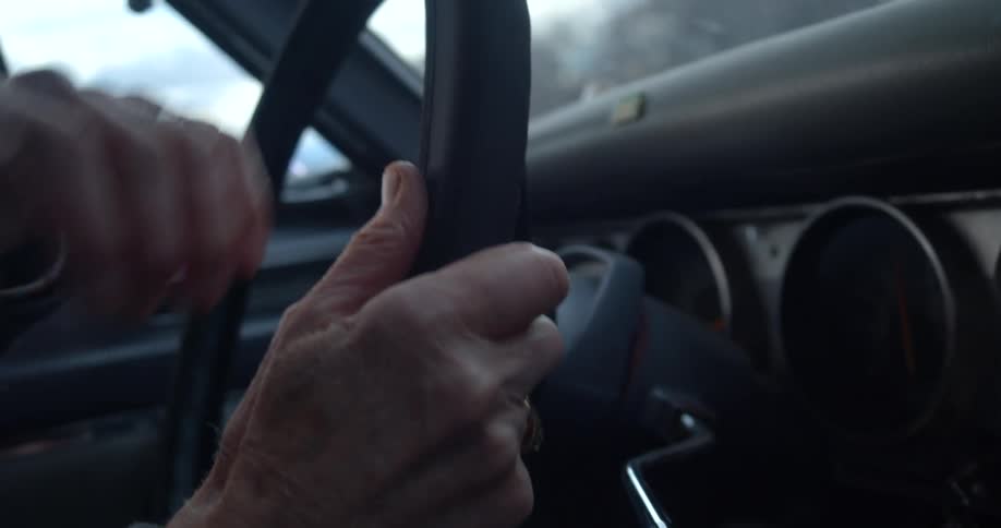 Close up of an elderly persons hands as they steer a car