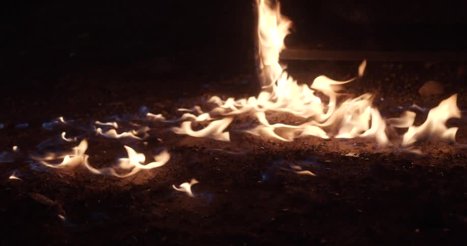 Flames burn across ground an on wooden furniture at night