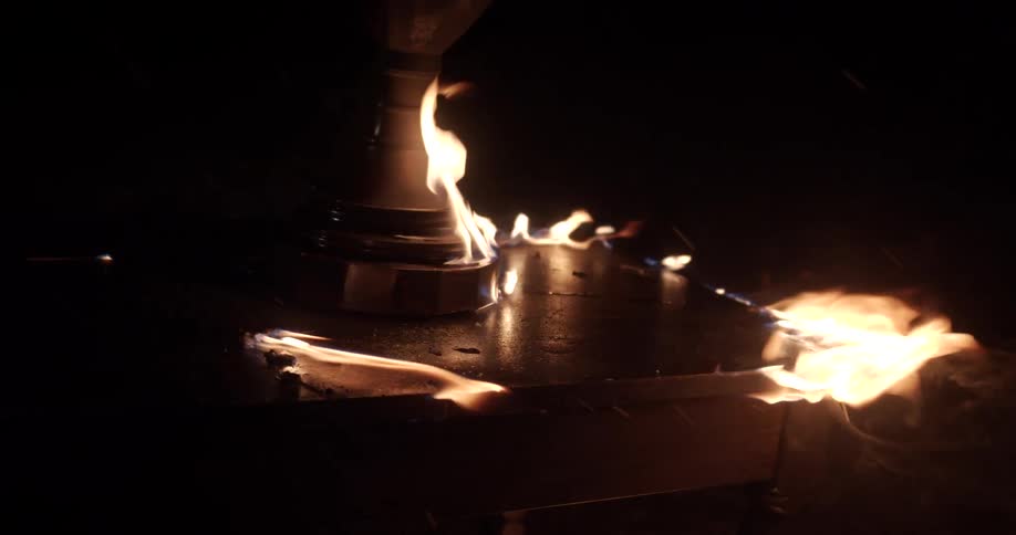 A wooden end table and lamp burn outside at night
