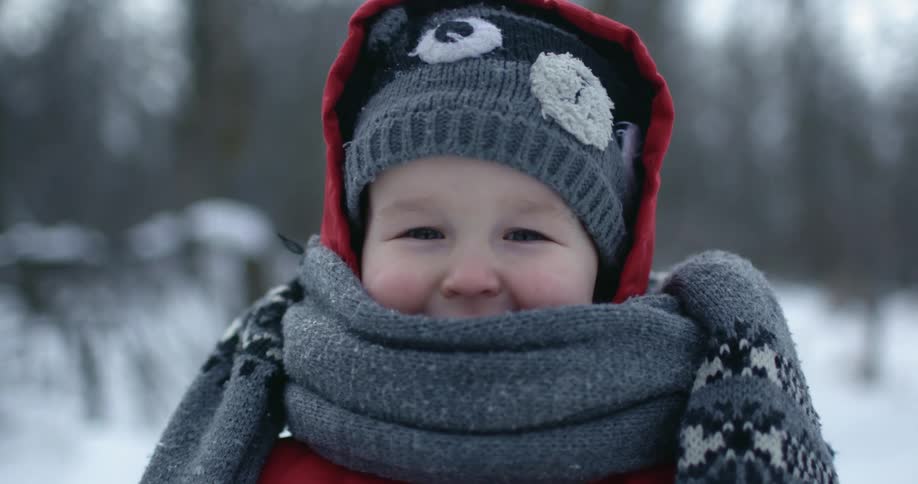 A toddler smiling while wrapped in a scarf outside on a freezing winter day